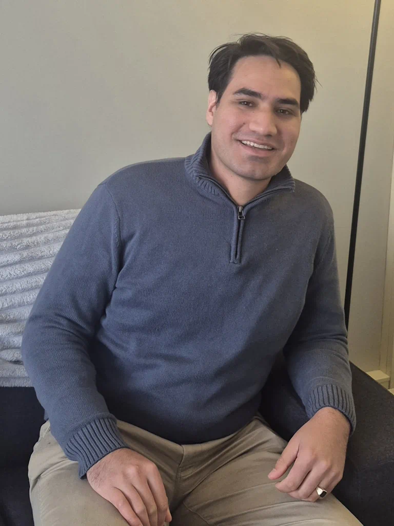 Smiling man in blue sweater seated indoors
