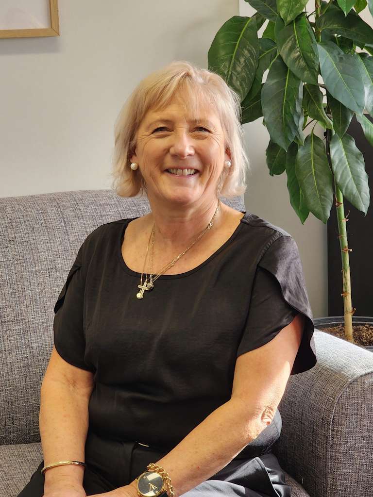 Smiling older woman seated on grey sofa indoors